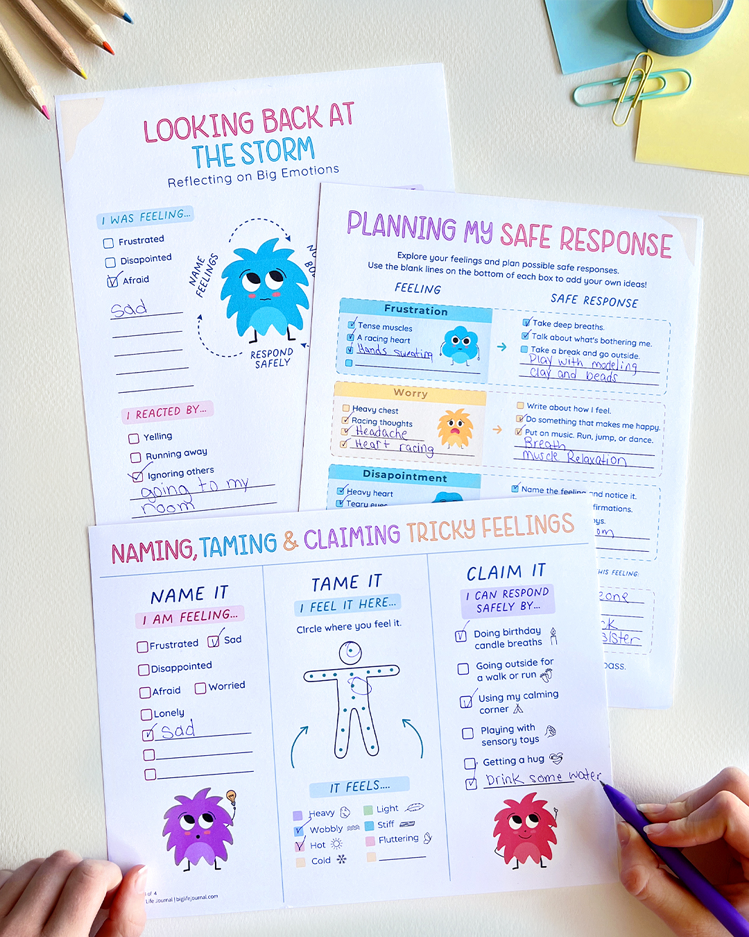 A person's hand filling out colorful worksheets about identifying and managing emotions with a purple pen.