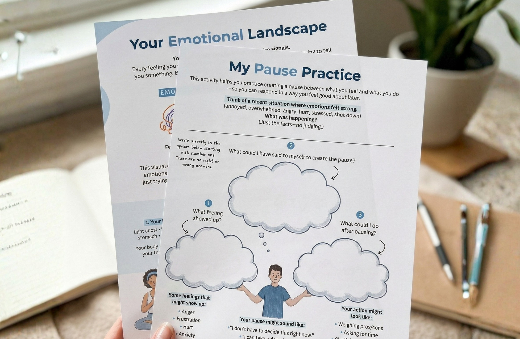 A person holds up two worksheets titled 'Your Emotional Landscape' and 'My Pause Practice' for managing feelings.