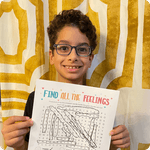 A young boy with glasses smiles while holding up a word search puzzle titled 'Find All The Feelings'.