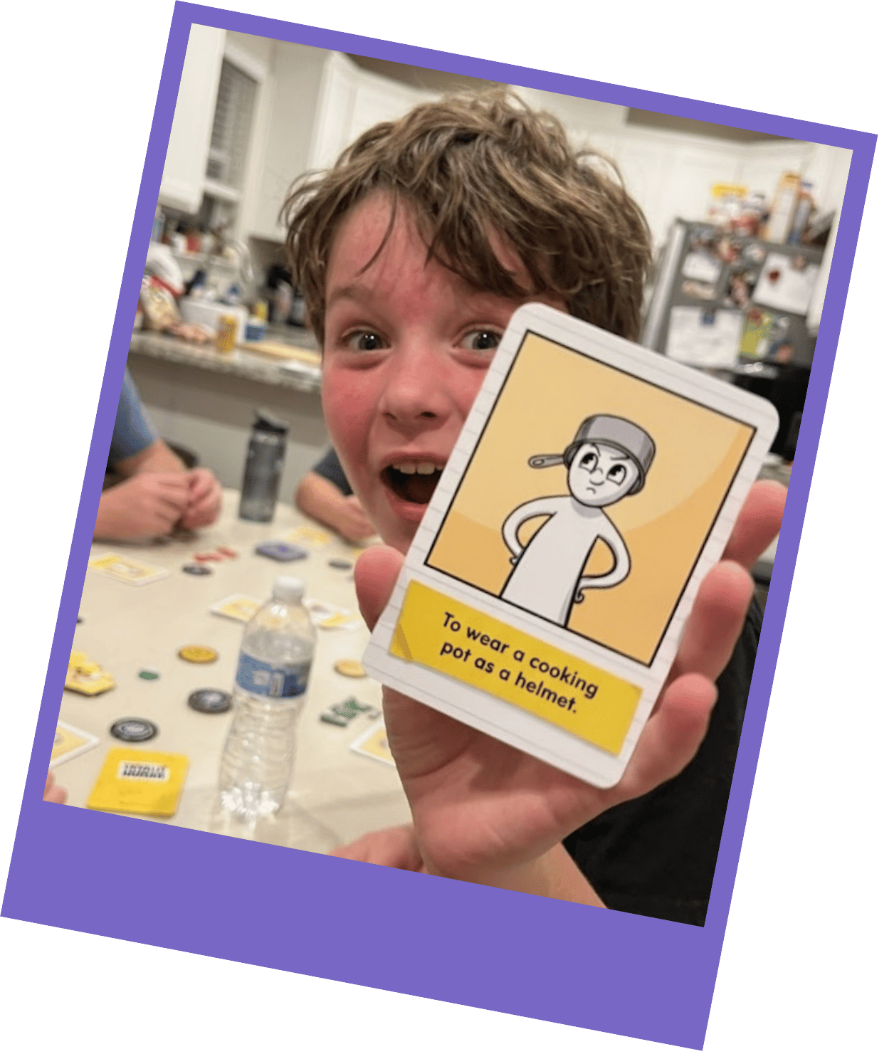 A boy with a surprised expression holds up a card game card that reads 'To wear a cooking pot as a helmet'.