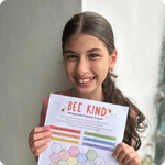 A smiling young girl holds up a printable chart with the words 'Bee Kind' at the top.