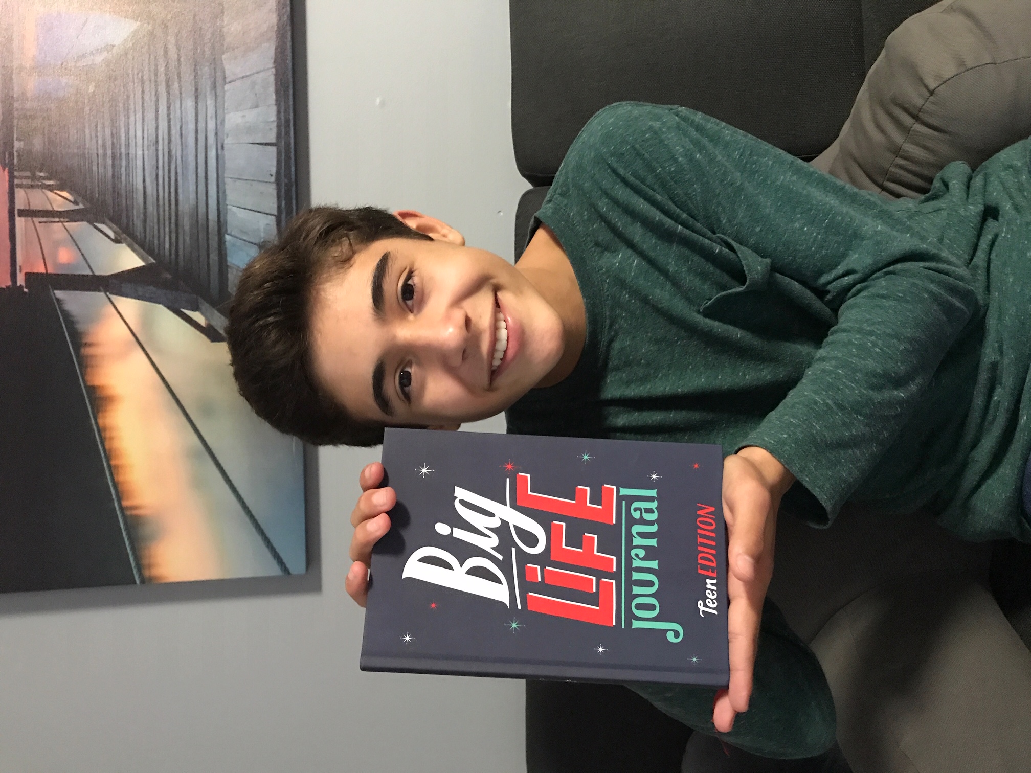 A smiling teenage boy holds up a copy of the 'Big Life Journal, Teen Edition'.