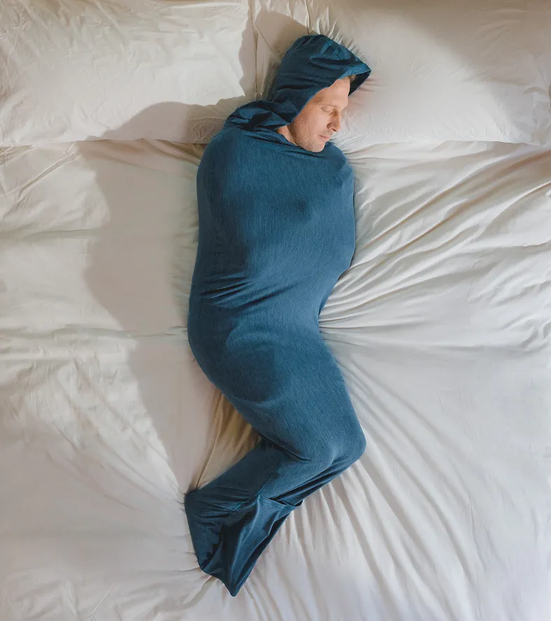 An overhead view of a person sleeping in a bed while encased in a blue hooded sleep sack.