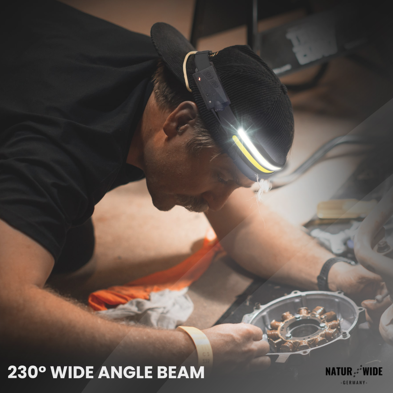 Person wearing a headlamp working on a mechanical part on the floor.