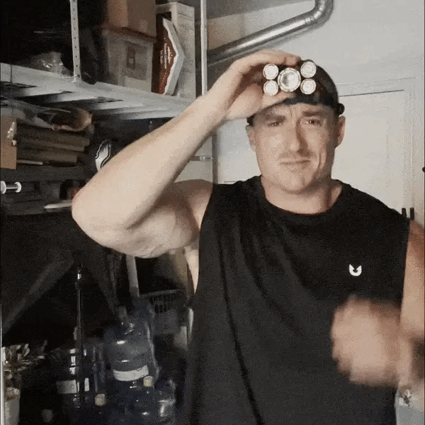 Man wearing a black tank top holding four batteries to his eyes like binoculars.