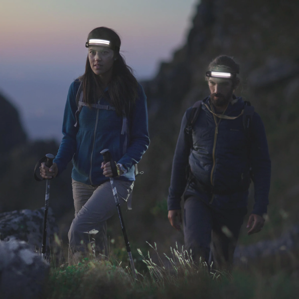 Two hikers walking with headlamps during twilight on a mountain trail.