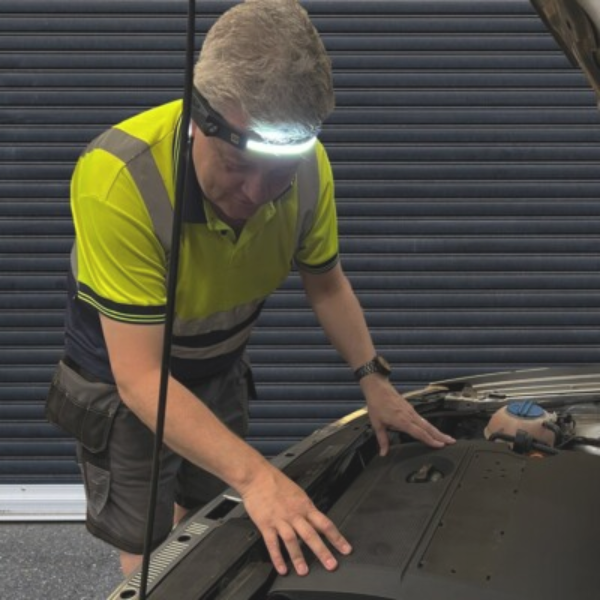 A person wearing a headlamp inspecting a car engine.