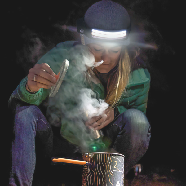 Person in a headlamp cooking outdoors, steam rising from a pot.