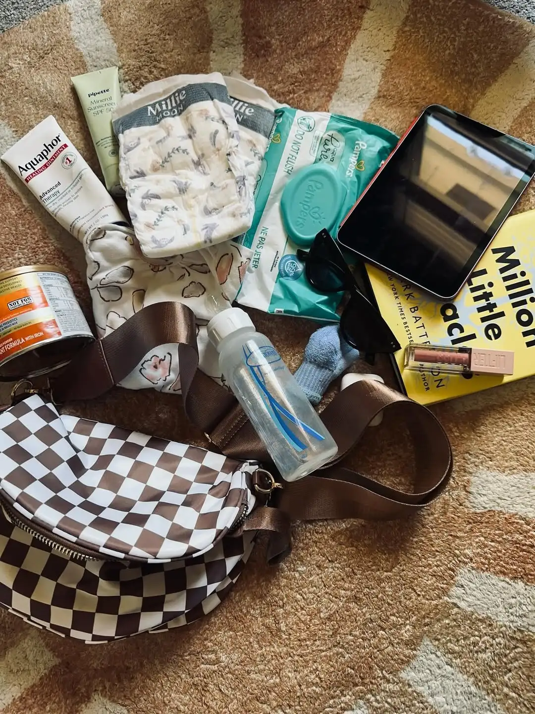 Assorted baby care items and a checkered bag on a patterned rug.