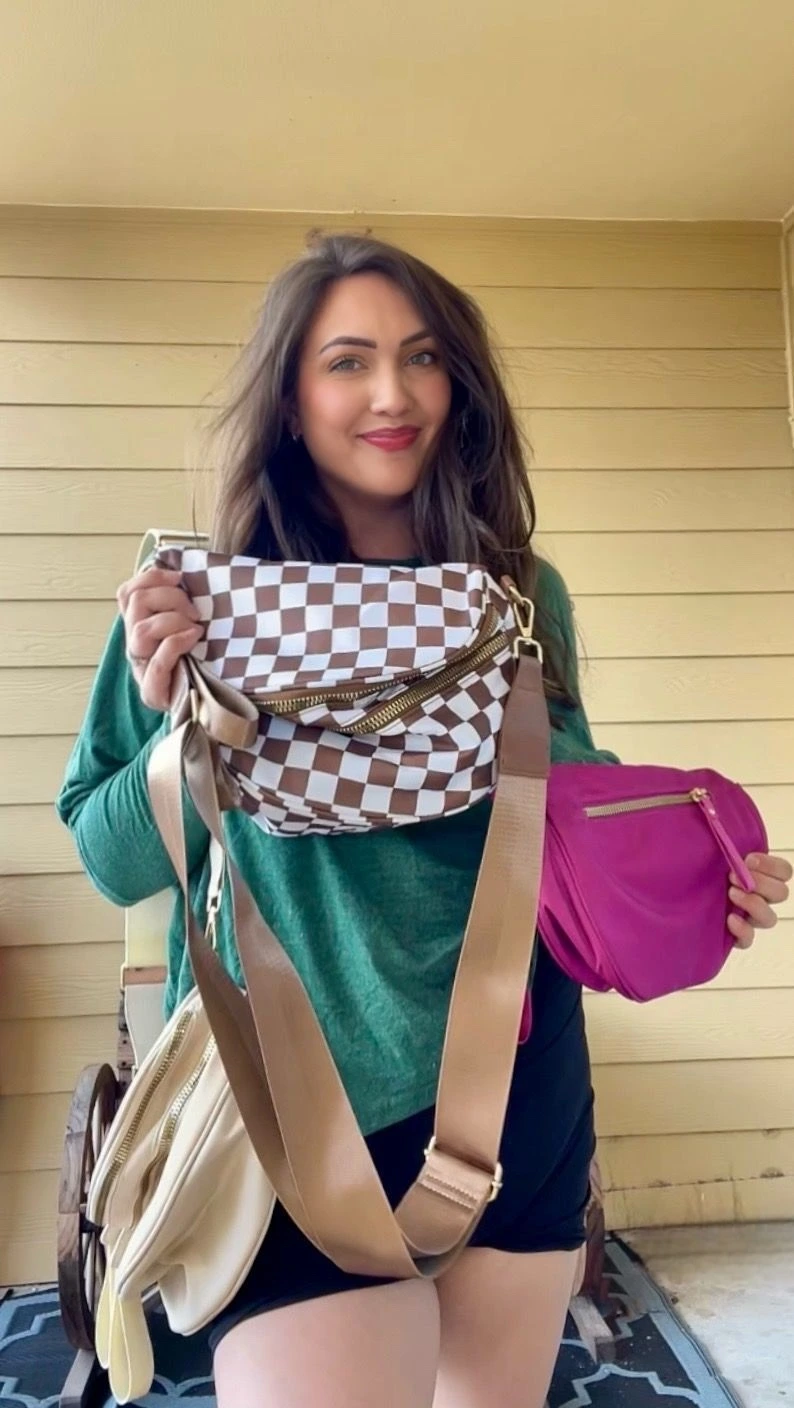 Person holding two bags, one checkered and one pink, while smiling outdoors.