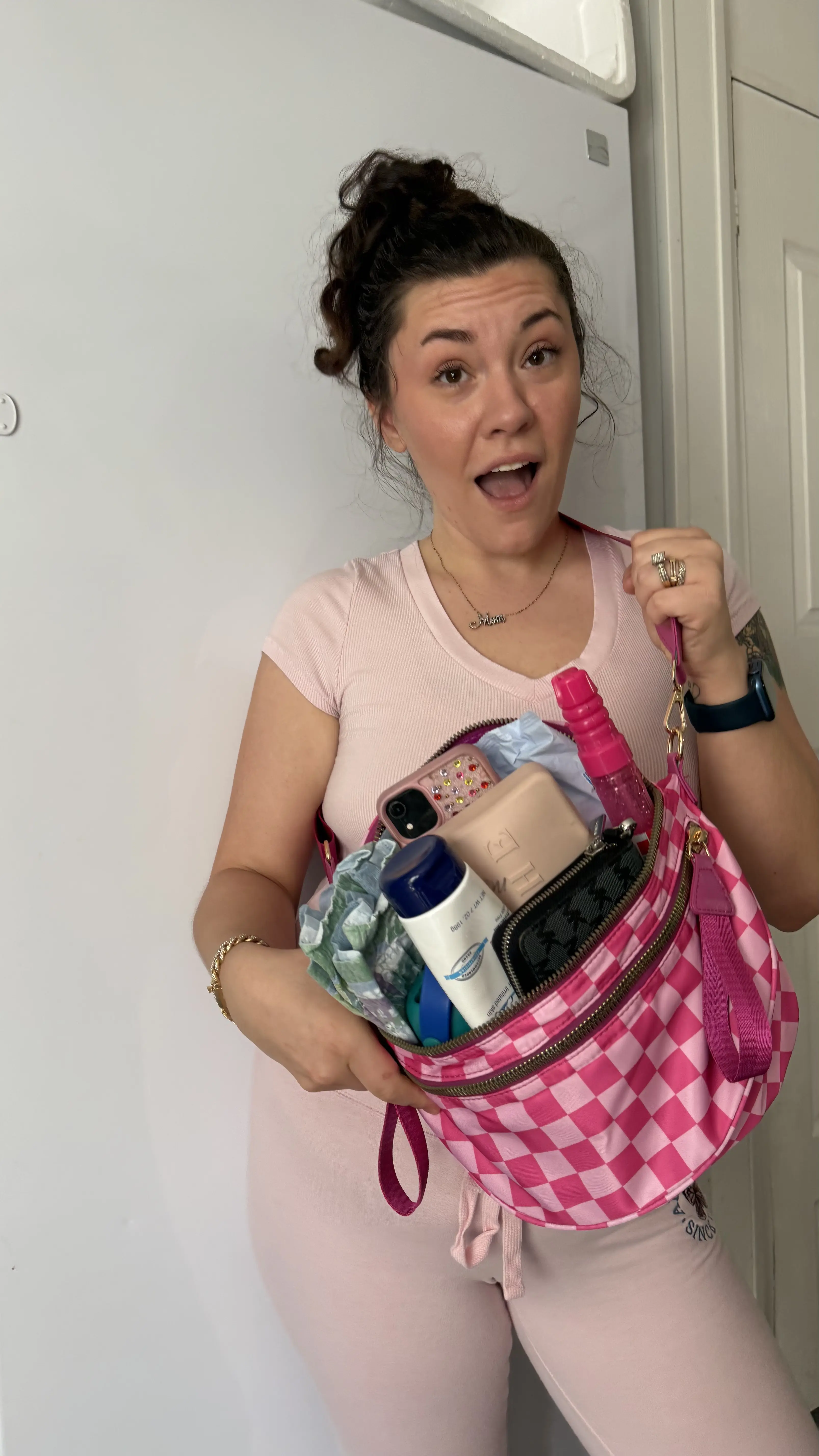 Person holding a pink checkered bag filled with various items, wearing a pink outfit.