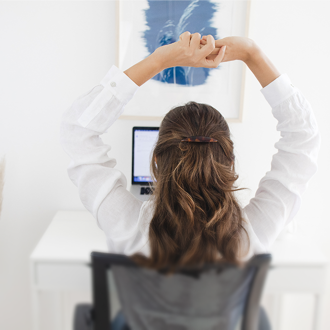 Person stretching at a desk with a computer and abstract art on the wall.