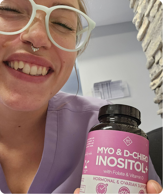 A smiling woman with glasses holds up a bottle of Myo & D-Chiro Inositol+ supplements.