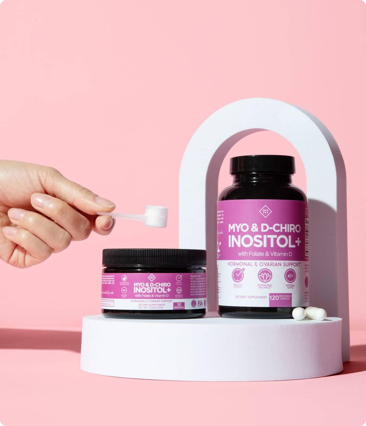 A hand scoops powder from a jar of Myo & D-Chiro Inositol+ next to a bottle of the same supplement.