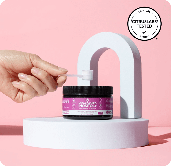 A hand holding a small scoop of white powder over a black jar of supplements on a pedestal.