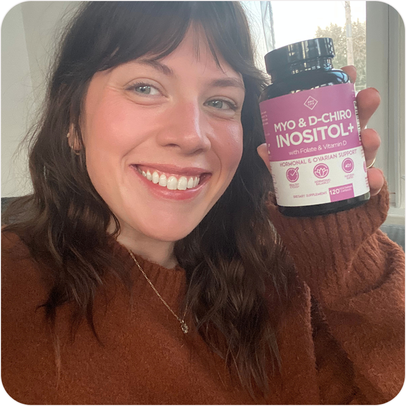 A smiling woman in a brown sweater holds up a bottle of Myo & D-Chiro Inositol+.