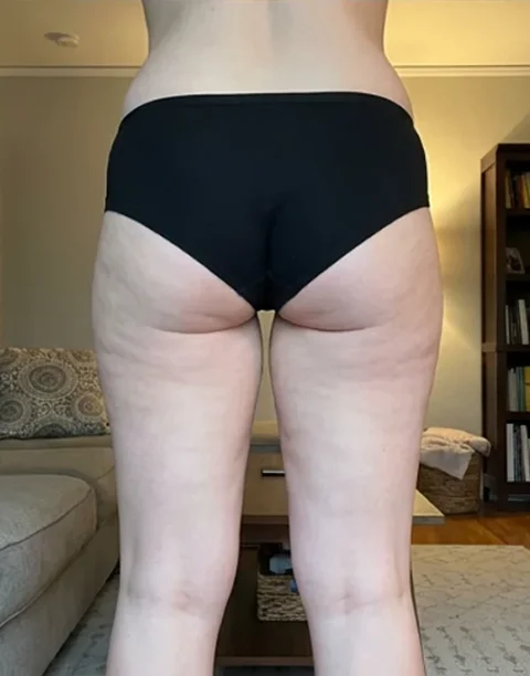 The back of a person's lower body, from the waist down, wearing black underwear in a room.