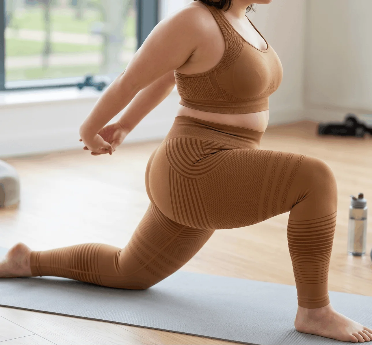 A person in a brown athletic set stretches in a lunge on a grey yoga mat.