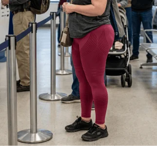 A person wearing red leggings and black sneakers waits in a line next to stanchions.