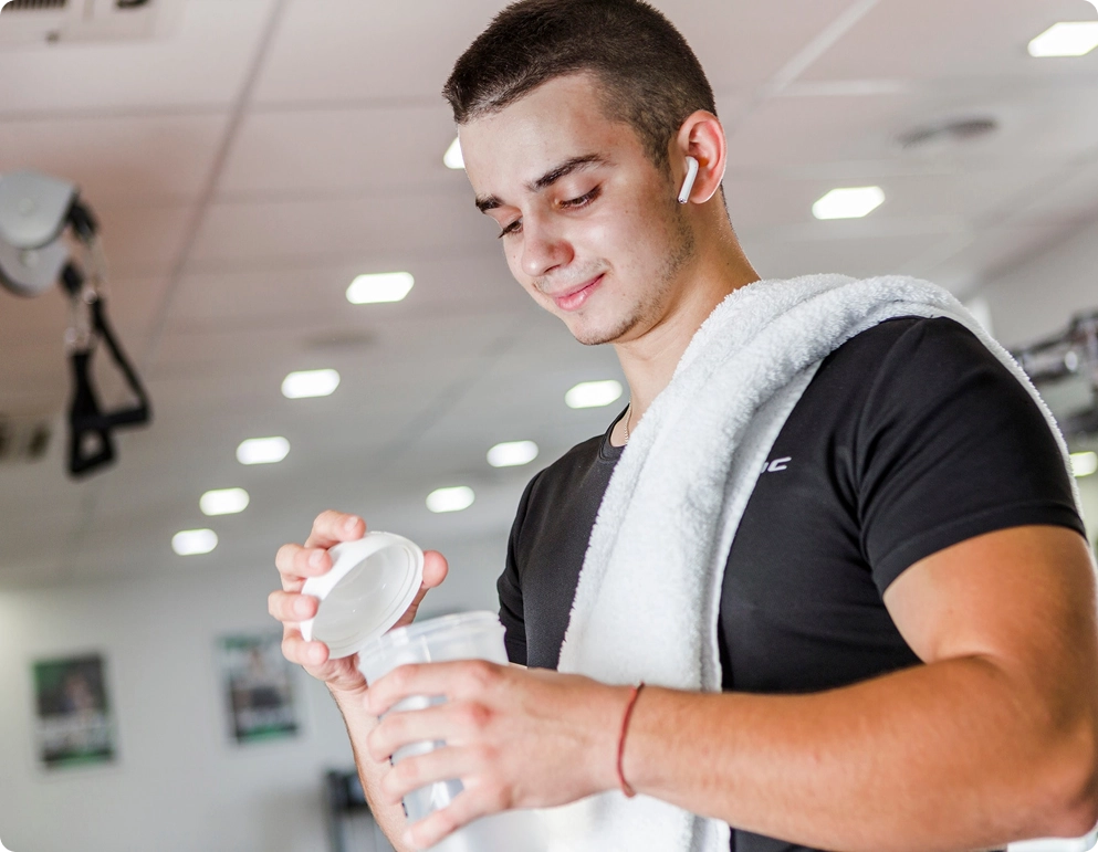 Man in gym with towel, opening a container.