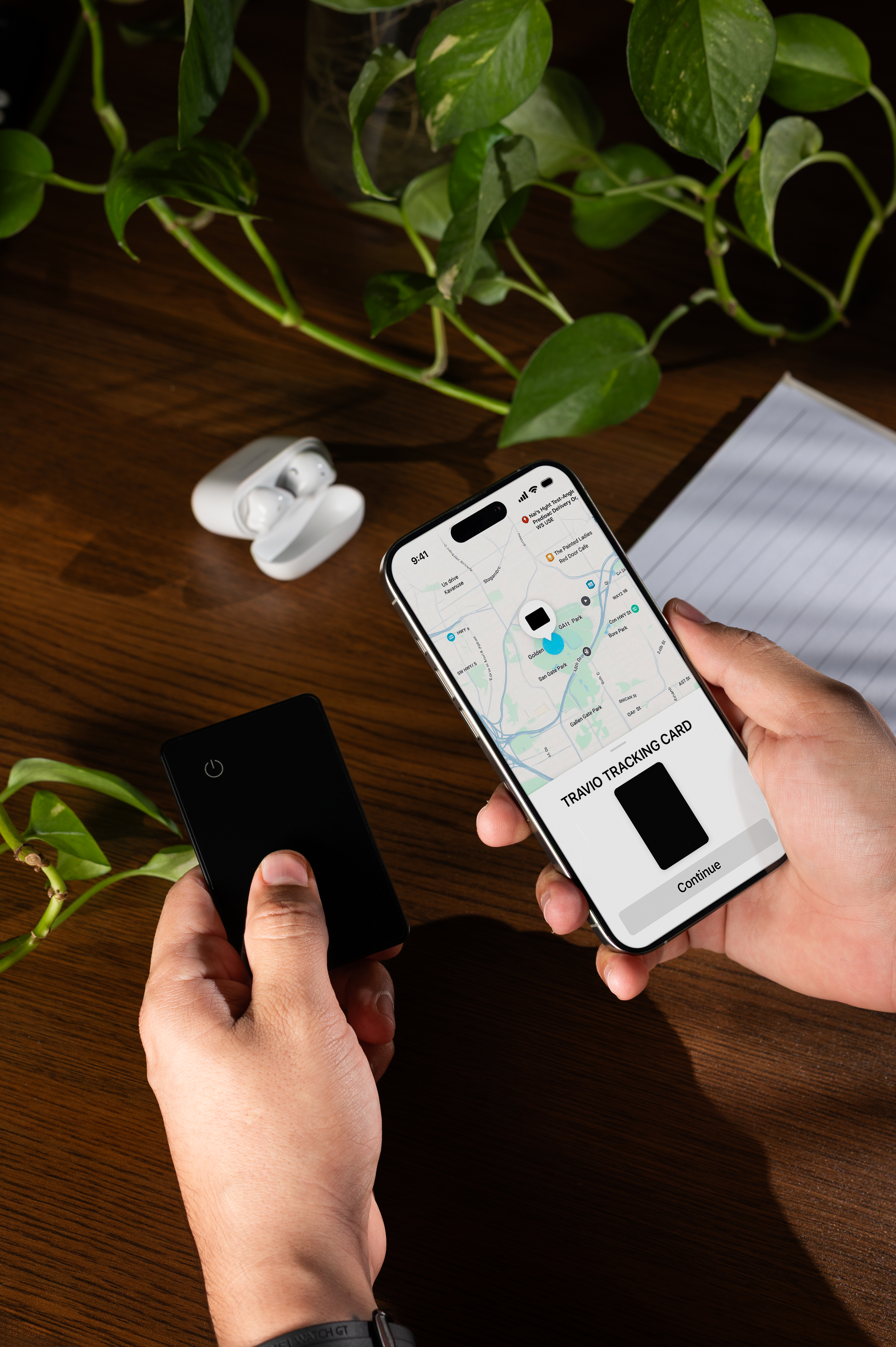 A person holding a smartphone and a black tracking card over a wooden desk with a plant.