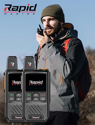 Person outdoors using a walkie-talkie, with two walkie-talkies in the foreground.