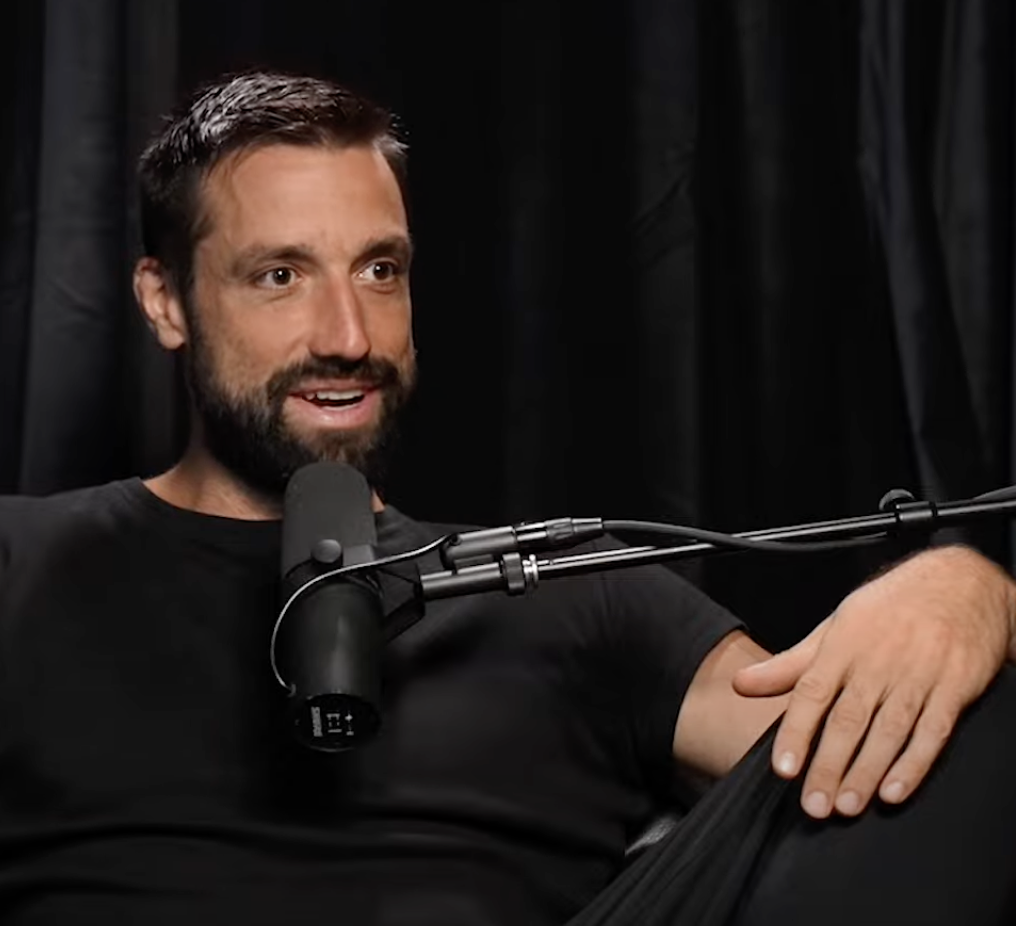 A person speaking into a microphone in front of a black curtain.