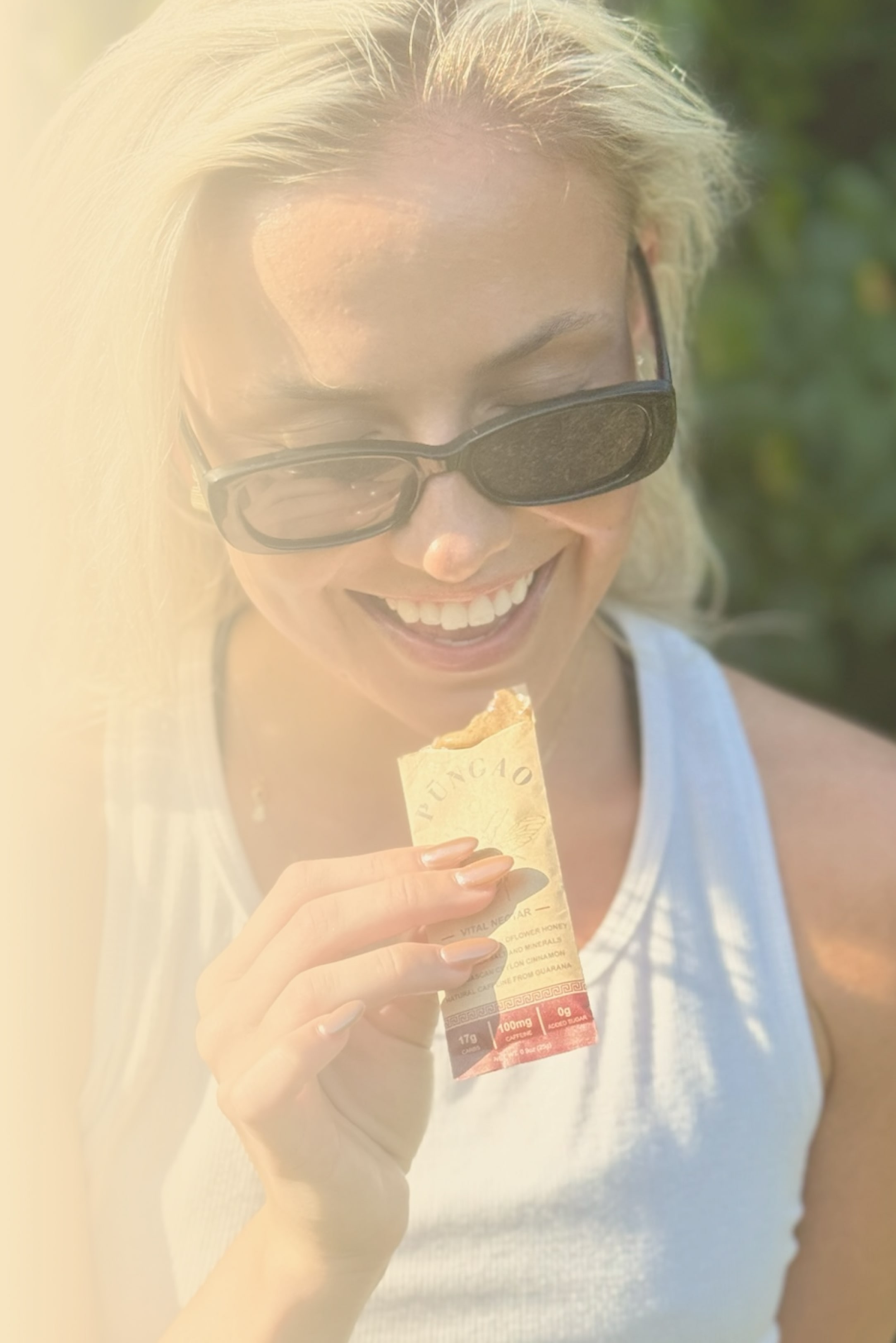 Person smiling while holding a snack bar outdoors.
