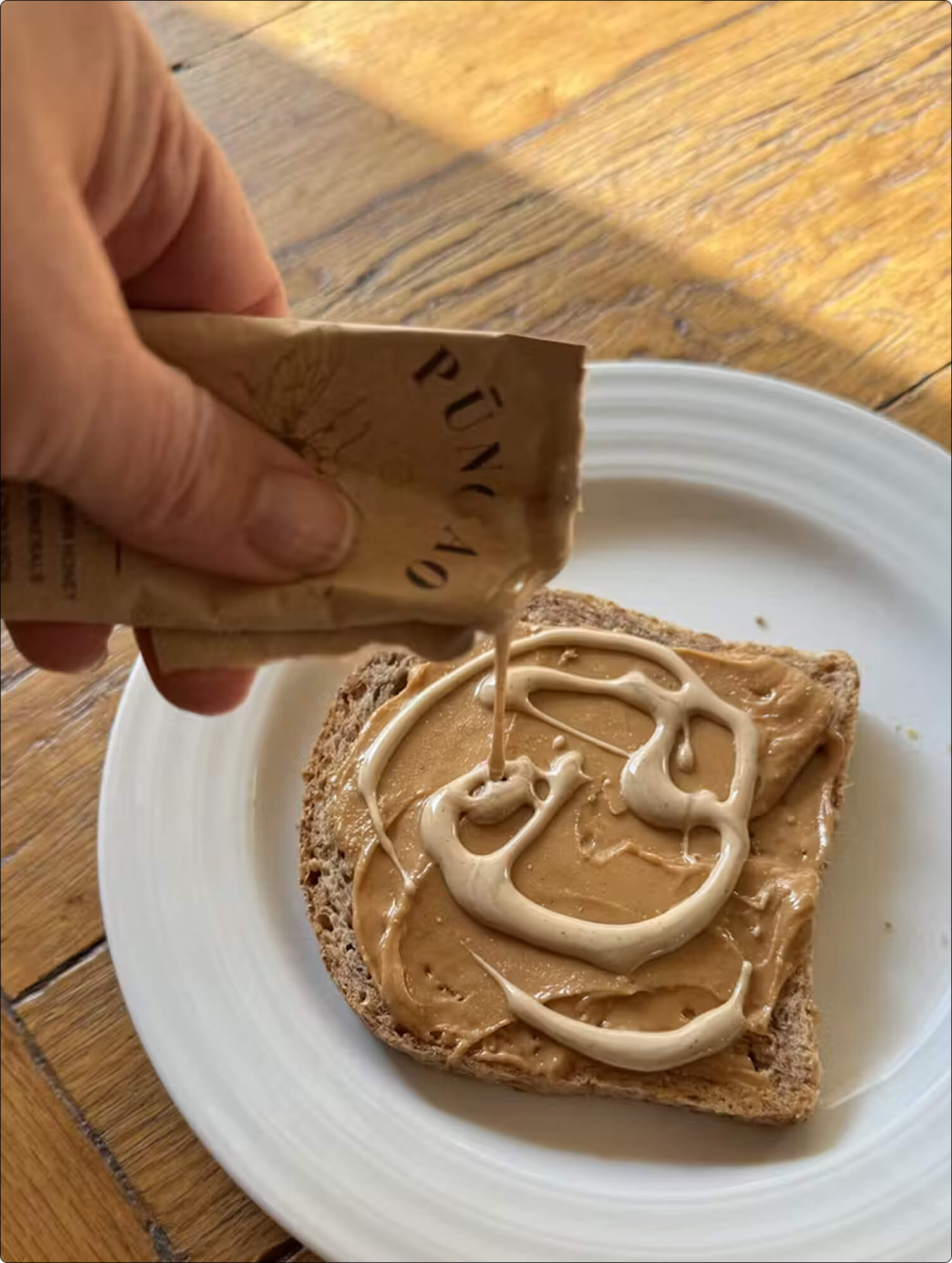 Hand pouring cream onto peanut butter toast on a white plate.