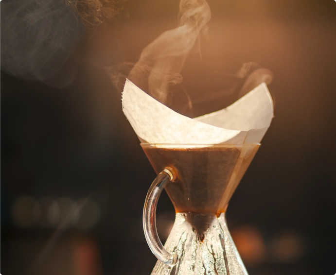 A close-up of steam rising from coffee brewing in a glass pour-over coffee maker with a paper filter.