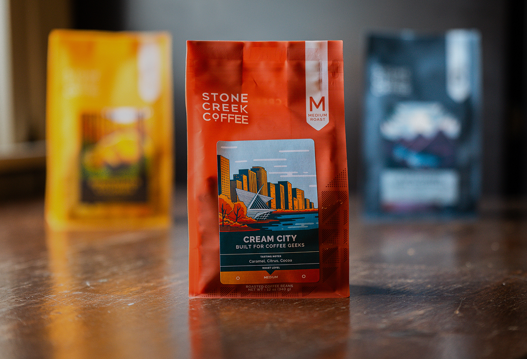 A red bag of Stone Creek Coffee's Cream City blend sits on a wooden table, with two other bags blurred in the background.