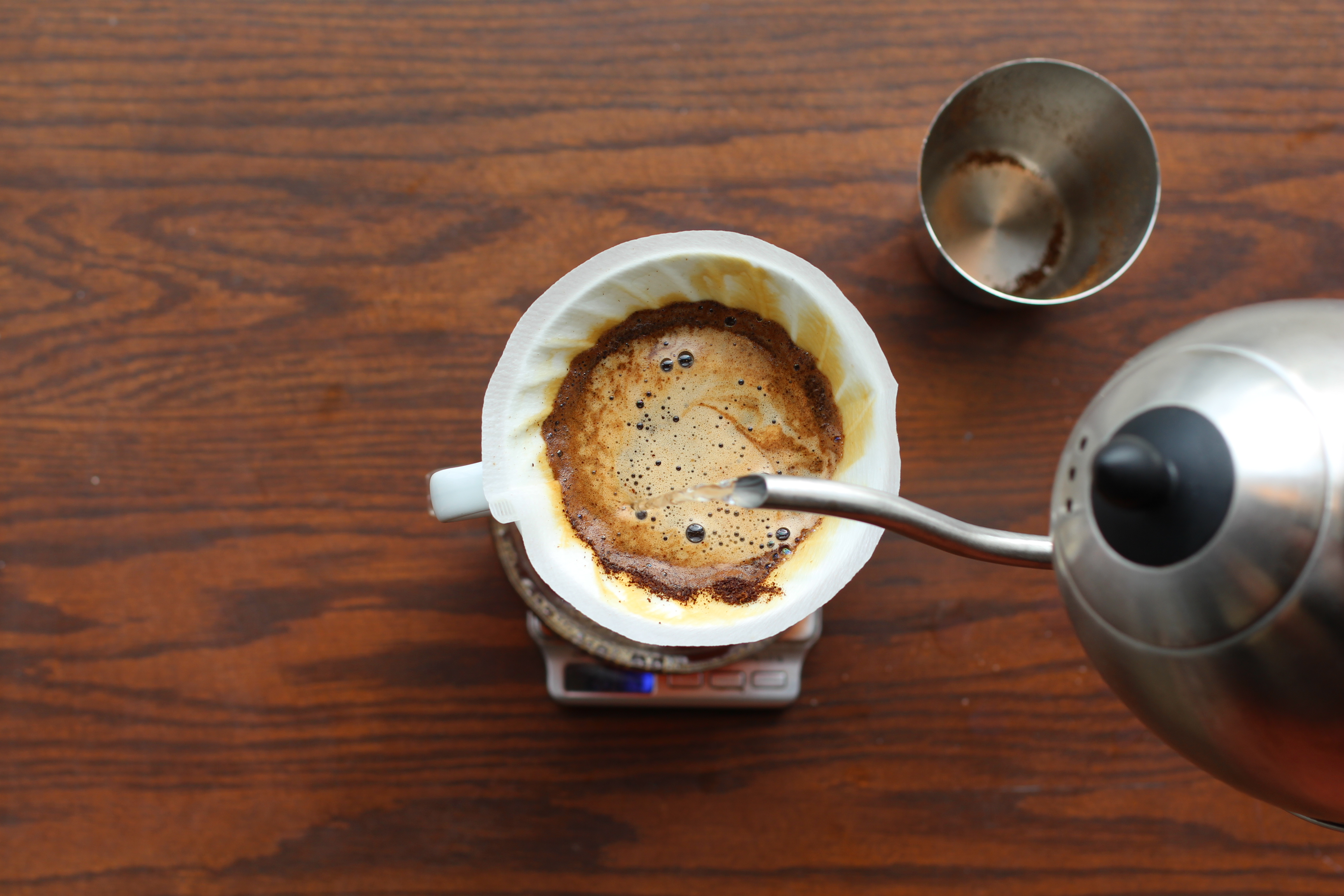 Pour-over coffee being made with a kettle and filter on a wooden table.