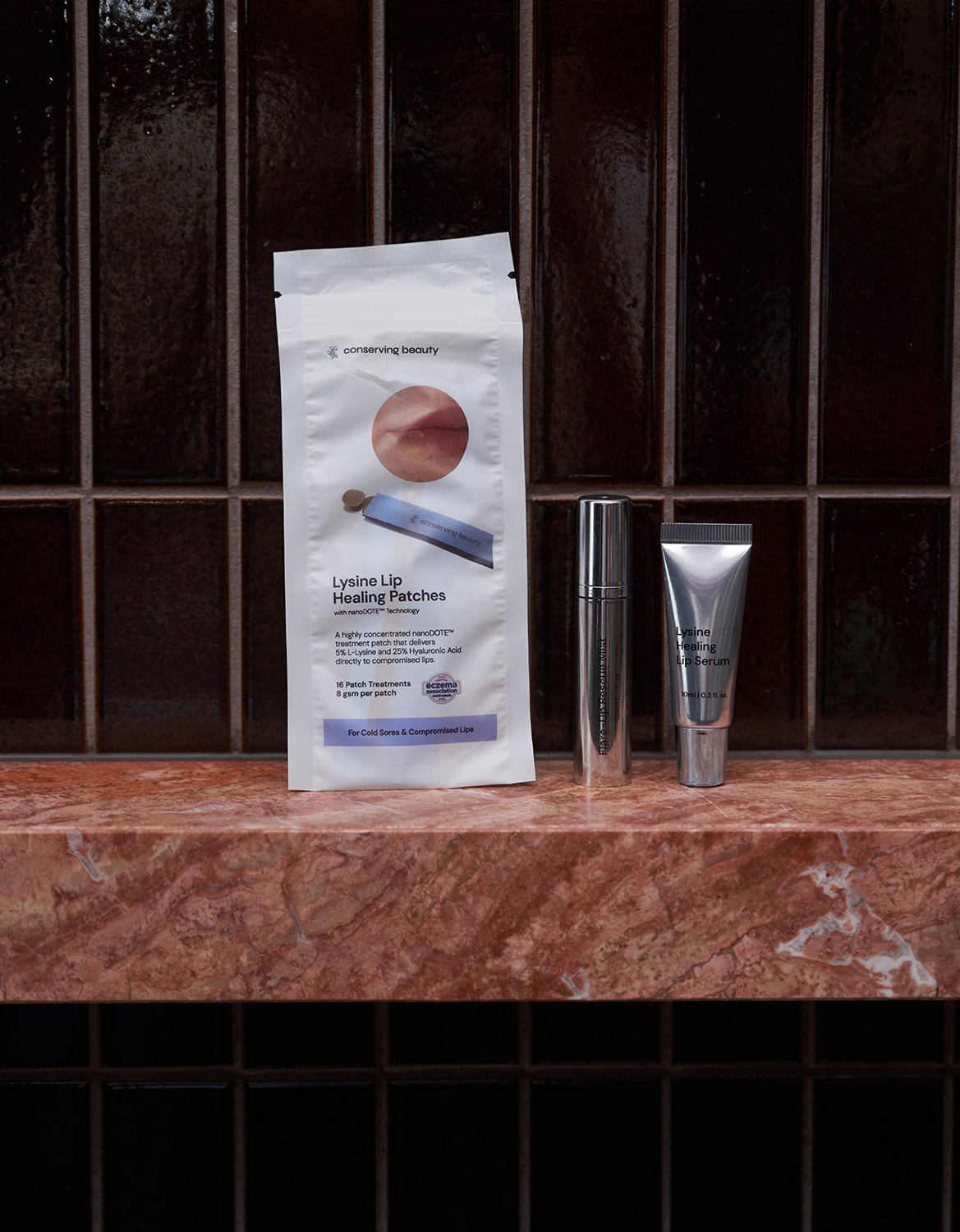 Conserving Beauty lip healing products displayed on a marble counter against a dark, tiled wall.