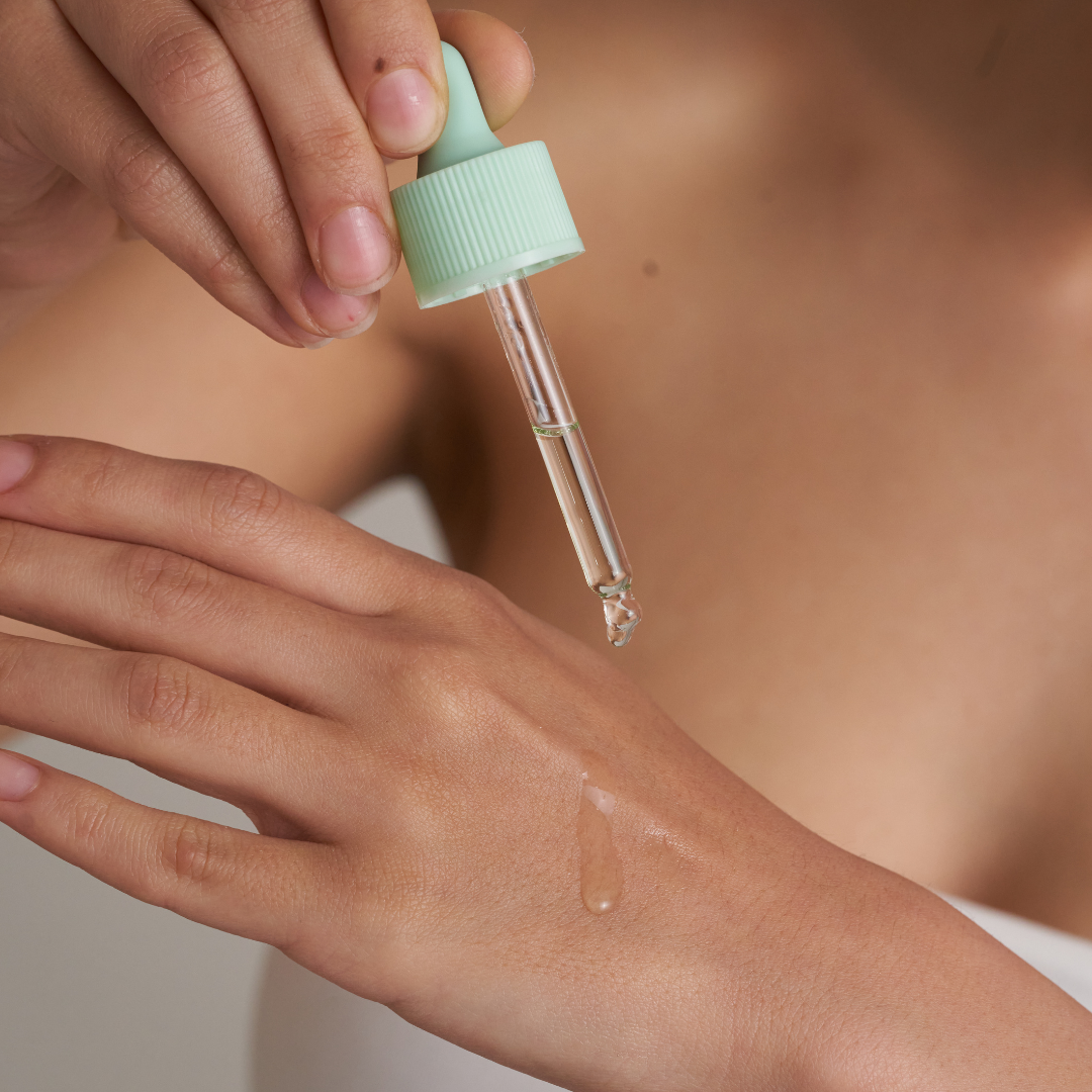 Hands applying serum with a dropper onto skin.