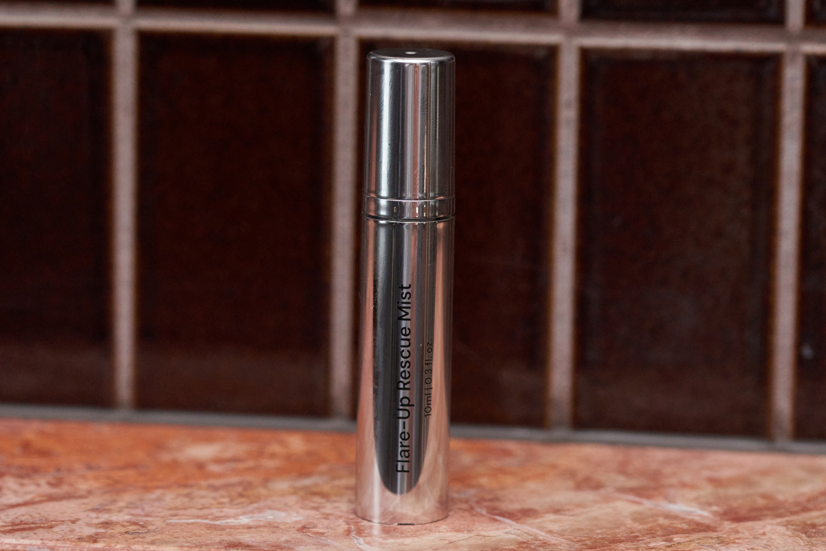A silver tube of Flare-Up Rescue Mist sits on a marble surface in front of a tiled wall.