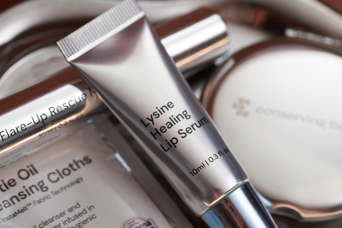 A close-up shot of a silver tube of Lysine Healing Lip Serum among other skincare products.