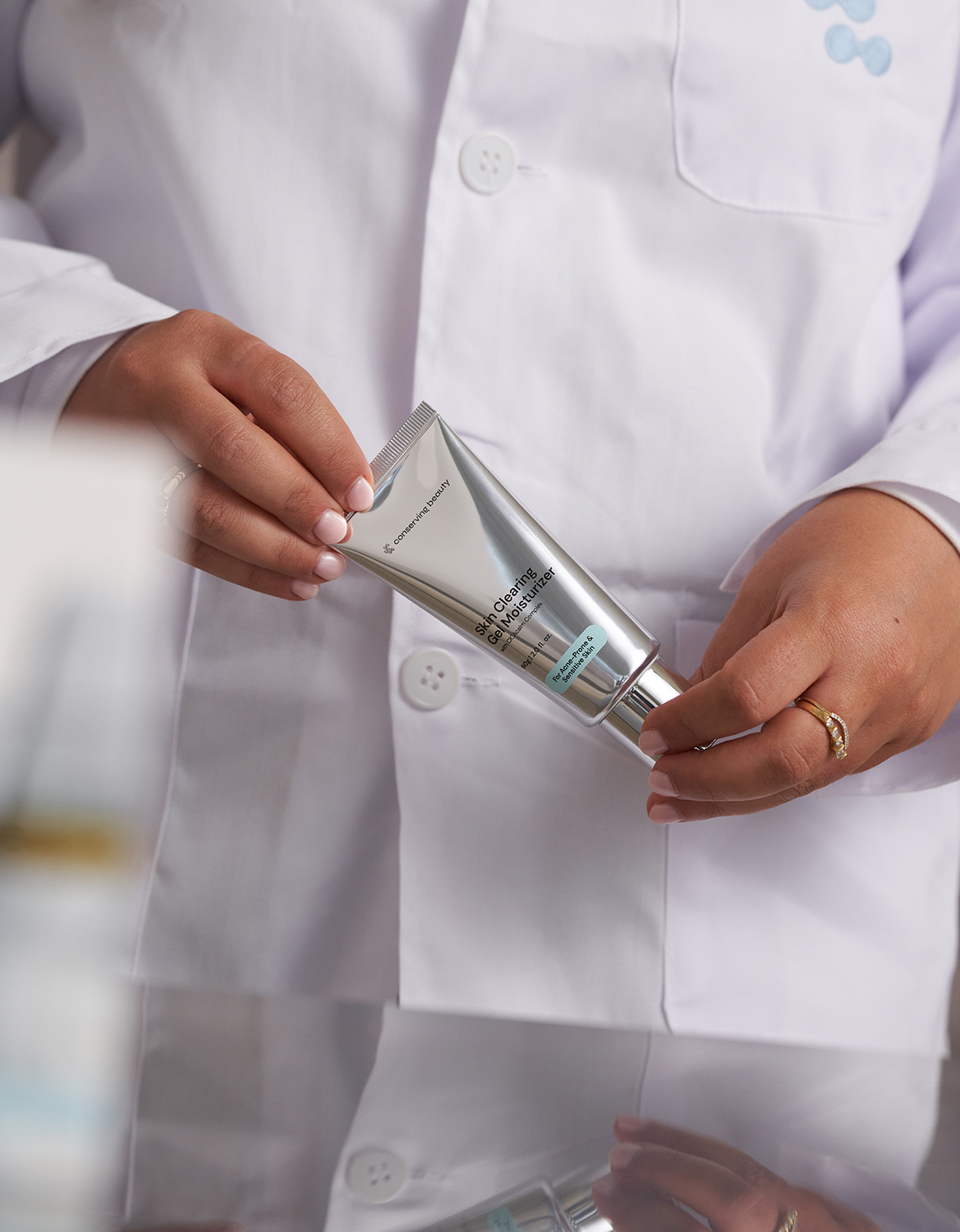 Person in a lab coat holding a tube of skincare product.