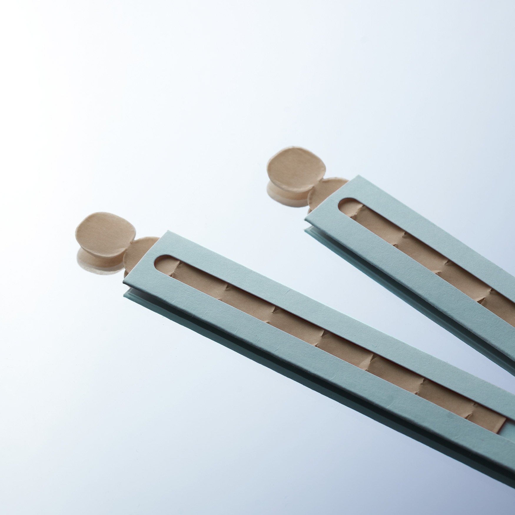 Two light blue paper strips with circular ends on a reflective surface.