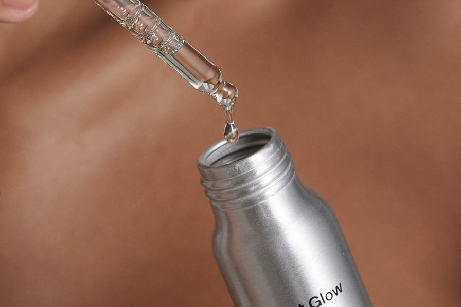 A close-up of a clear liquid being dispensed from a glass dropper into a silver bottle.