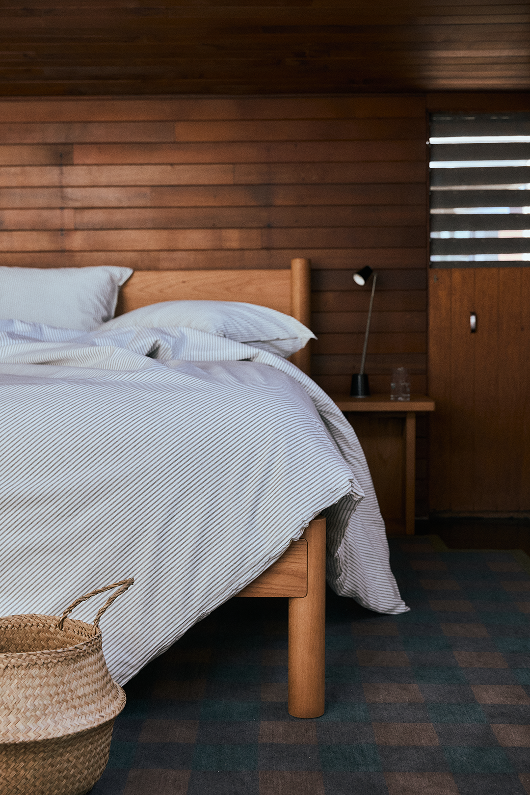 A wooden bed with a striped duvet cover in a room with wood-paneled walls.