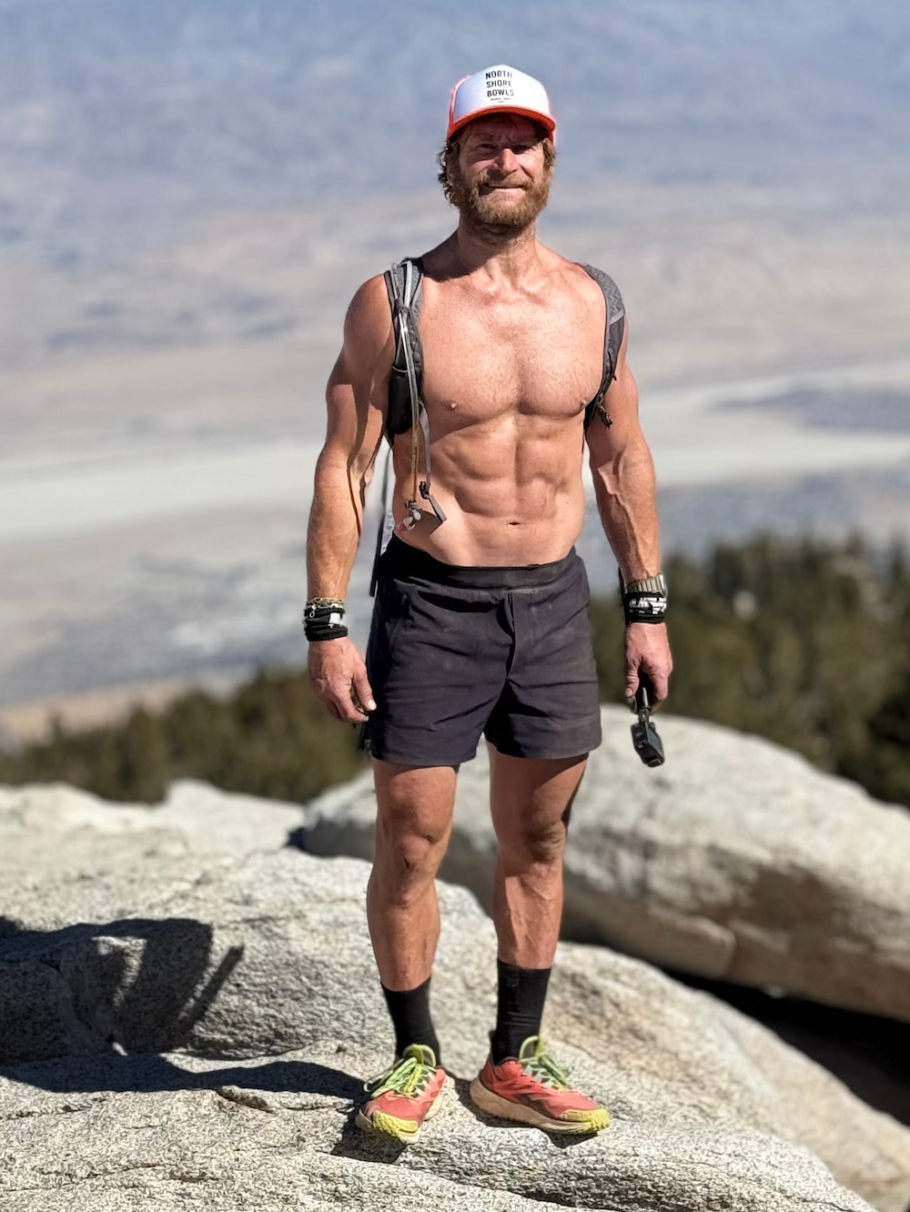 Man in athletic gear standing on rocky terrain with a mountainous background.