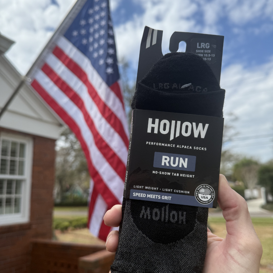 A hand holds up a package of Hollow performance socks in front of an American flag.