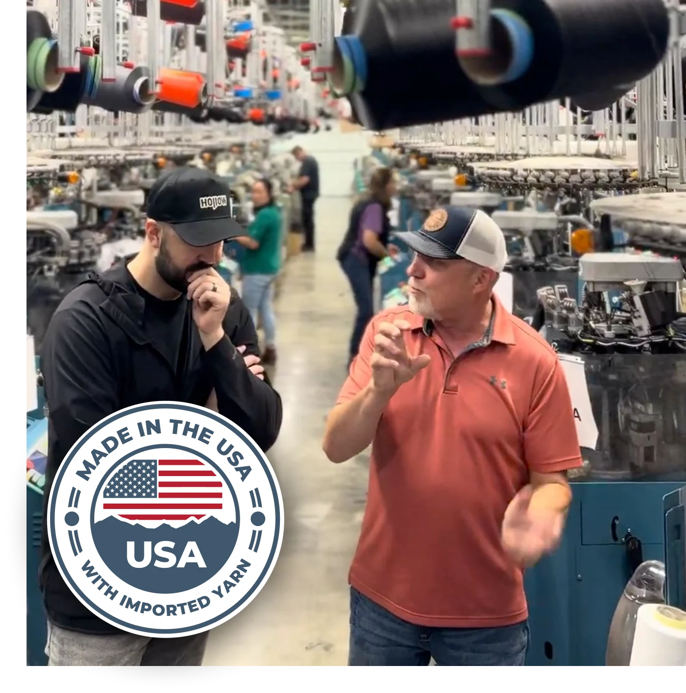 Two men talking in a textile factory, with machines and a 'Made in the USA' badge.
