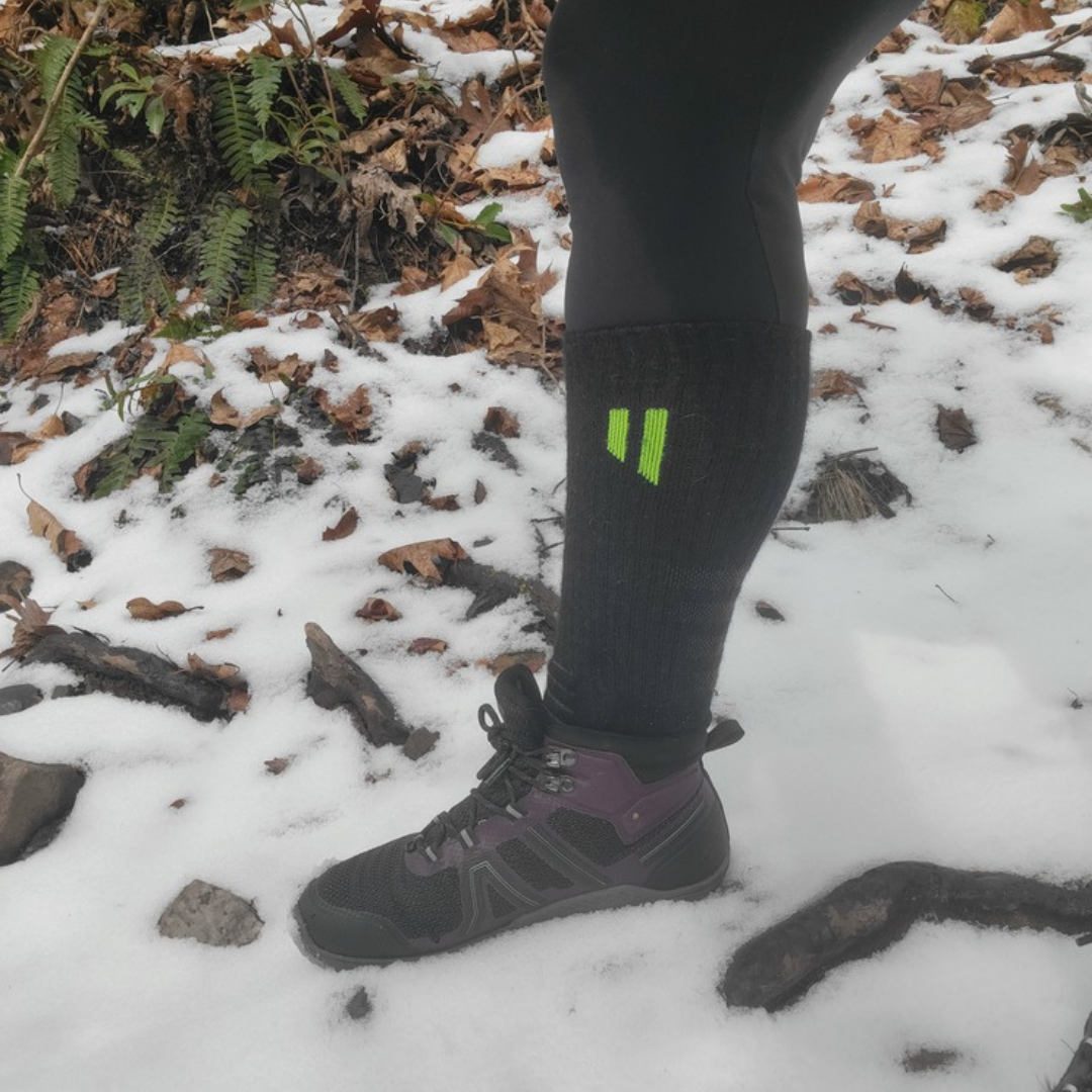 A close-up of a person's leg in a hiking boot and sock standing in the snow.