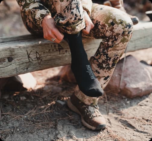 Person in camouflage clothing putting on black socks.