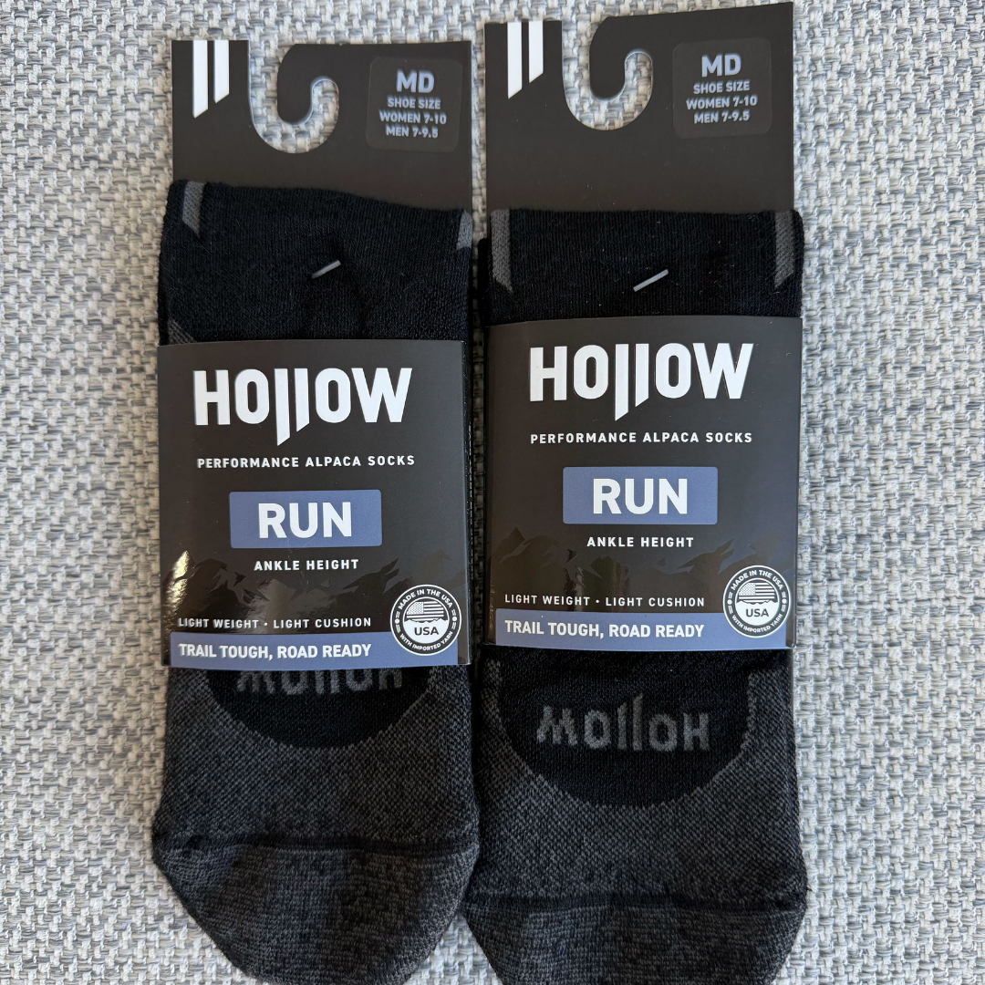 Two pairs of new Hollow brand black ankle-height running socks laid flat in their packaging.