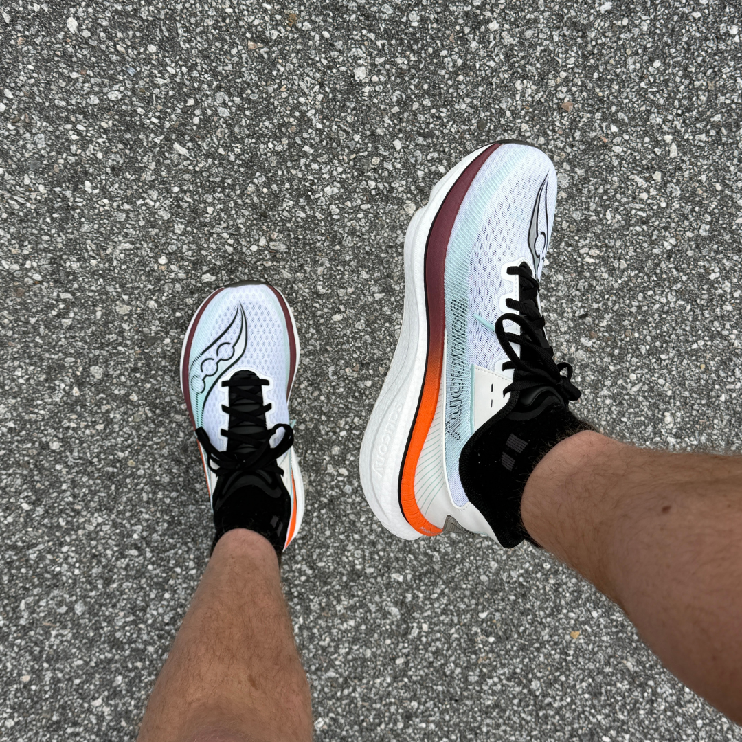 A first-person view looking down at a pair of white Saucony running shoes on asphalt.