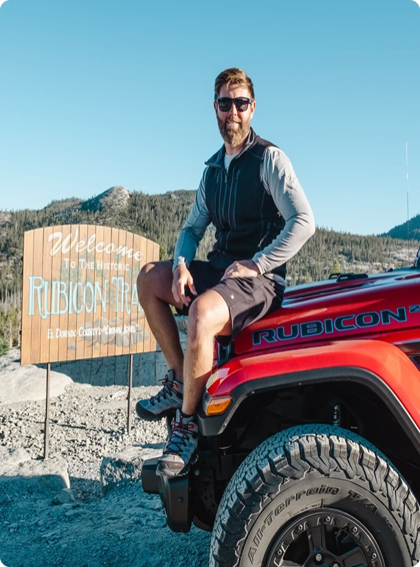 Man sitting on a red Jeep near Rubicon Trail sign.