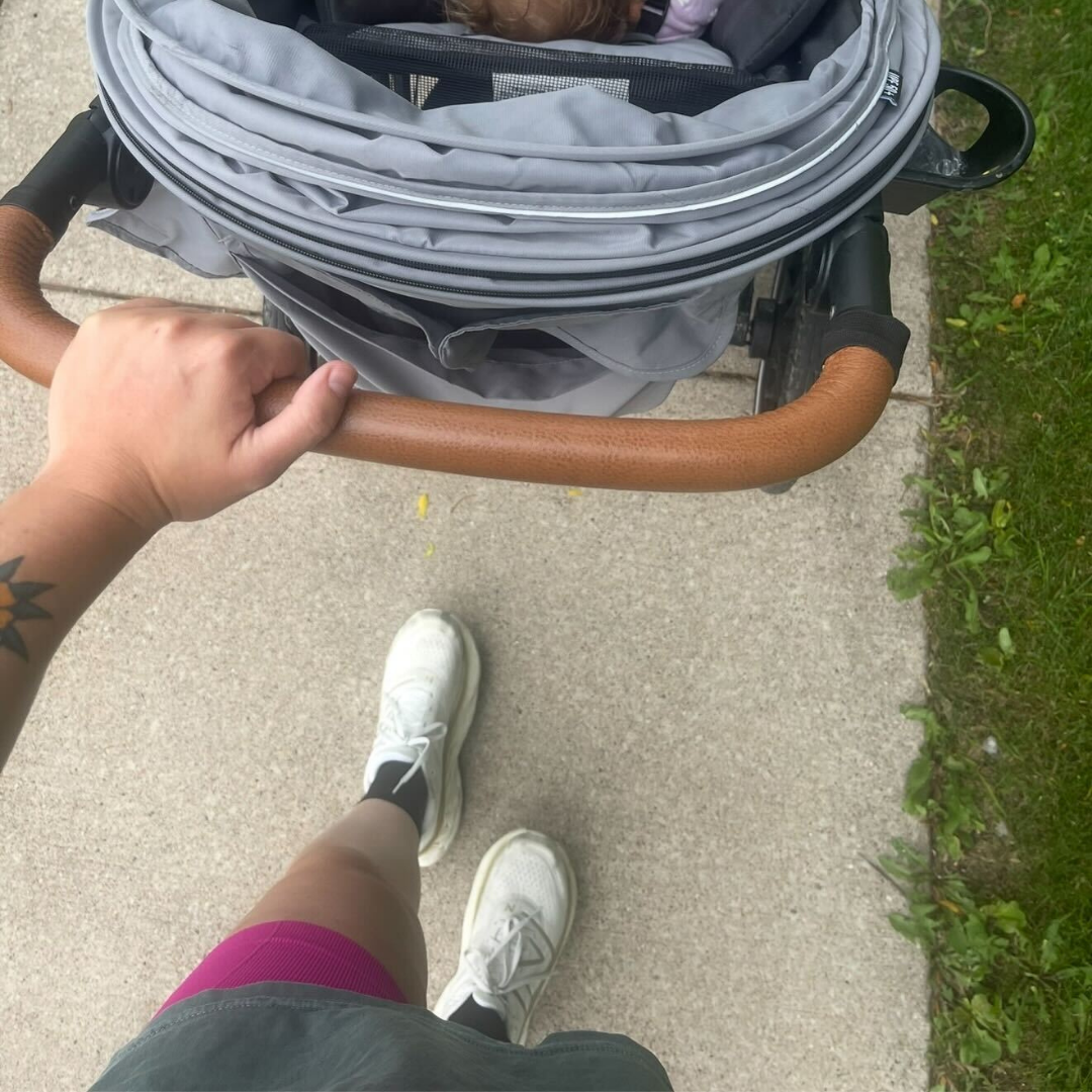 A first-person view of someone pushing a grey baby stroller on a sidewalk.