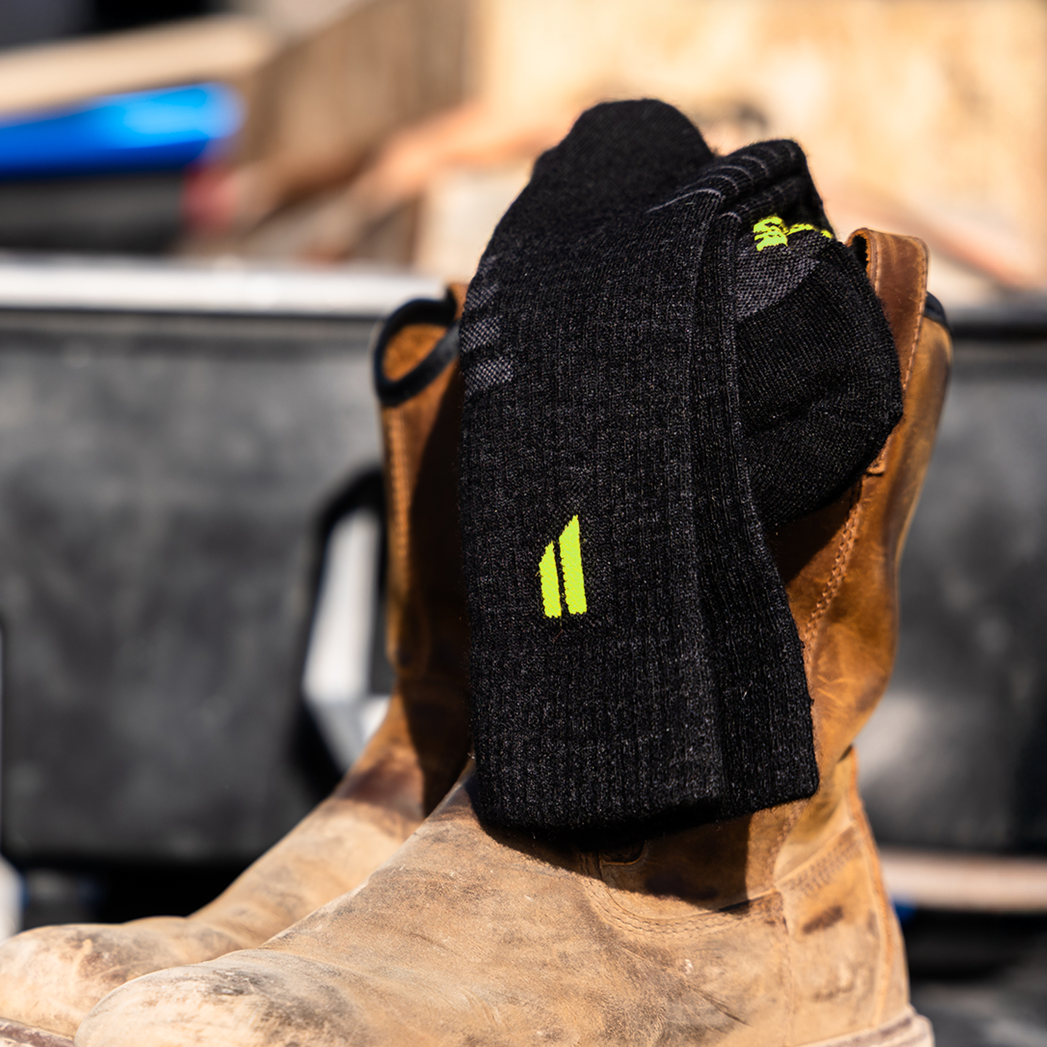 A pair of black socks with a neon green logo draped over a pair of brown leather work boots.